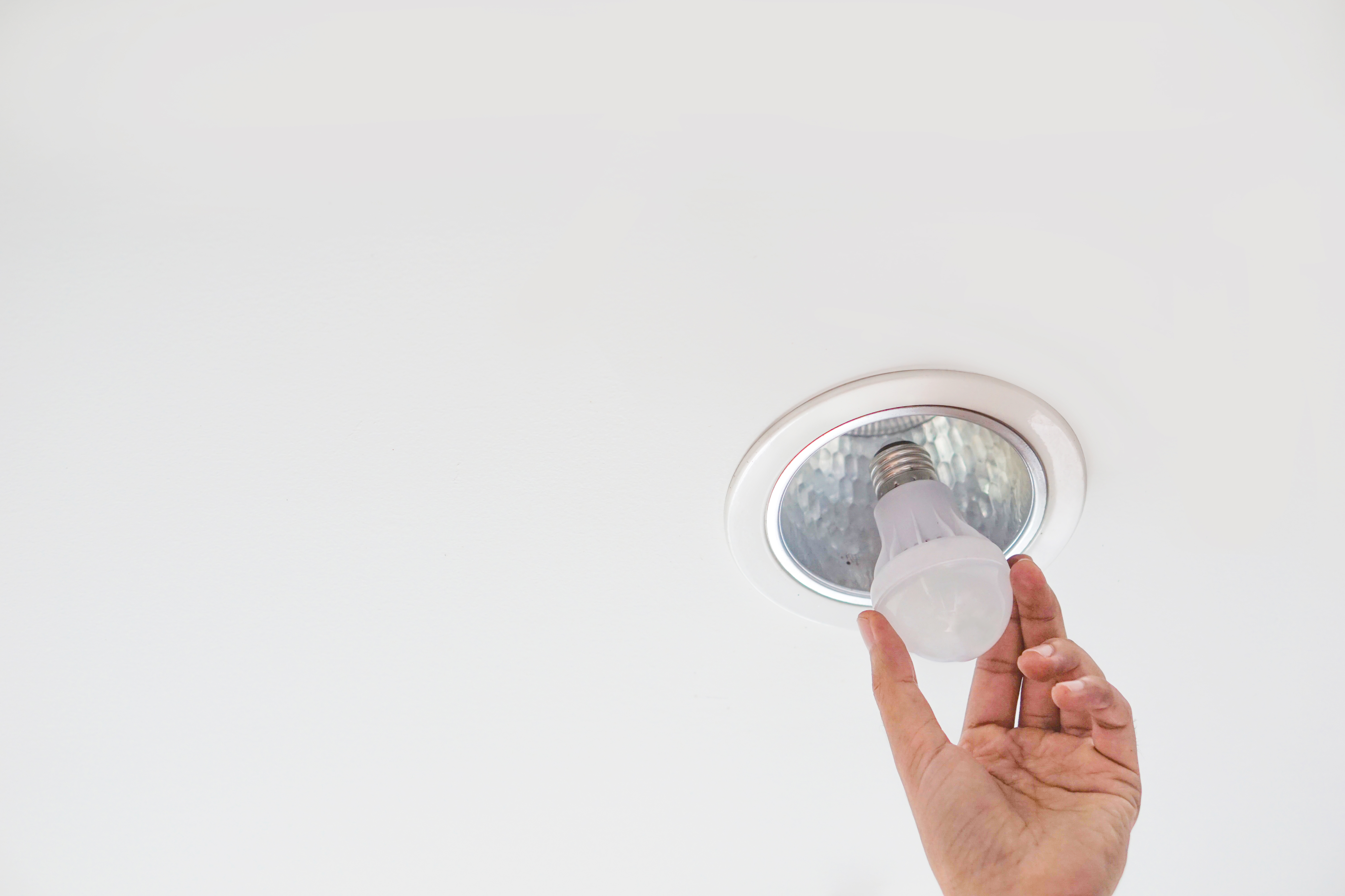 Cropped Hand Of Person Holding Bulb By Ceiling